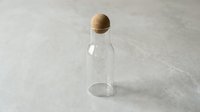 Empty glass bottle with cork stopper on neutral concrete surface, suitable for product mockups, storage solutions, and eco-friendly packaging designs.