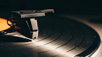 Vintage turntable with tonearm and stylus playing vinyl record in warm atmospheric lighting for music and audio production concepts.