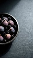 Fresh figs and blackberries in rustic bowl on dark slate surface, overhead view. Ideal for food styling, culinary blogs, recipe websites, and gourmet food marketing.
