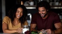 Happy young African American couple laughing together while preparing healthy meal with fresh ingredients in modern kitchen at home.