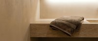 Folded brown towel resting on wooden shelf in minimalist bathroom interior with neutral beige walls and natural lighting for spa and home decor projects.
