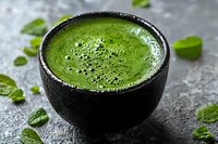 Fresh green smoothie with chia seeds in dark ceramic bowl surrounded by mint leaves on stone surface for healthy lifestyle and nutrition concepts.