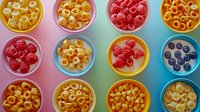 Colorful bowls filled with fresh raspberries, blueberries and crunchy cereal rings on gradient background. Healthy breakfast concept for menu design.