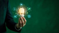 Businessman hand holding glowing lightbulb with green technology icons on emerald background representing innovation and sustainable business solutions.