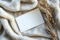 Blank white card mockup on natural linen fabric with dried wheat stalks, creating rustic composition for wedding stationery or autumn greeting design.