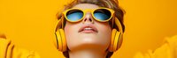 Young woman in yellow sunglasses and headphones looking up against vibrant orange background, expressing joy and modern lifestyle. Perfect for music and fashion advertising.