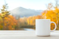 White coffee mug mockup on wooden table against blurred autumn mountain landscape background with golden foliage and lake view, copy space for branding design.