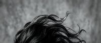 Dramatic black and white portrait of flowing hair in motion against textured background. Hair movement and dynamic styling concept for beauty campaigns.