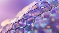Macro view of water droplets on mesh net structure with purple and blue bokeh background creating abstract pattern of hexagonal shapes and light reflections.
