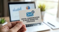 Hand holding business card with digital communication and online marketing strategies text, laptop displaying charts in background for professional services.