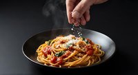 Hand sprinkling cheese over delicious spaghetti pasta with tomato sauce in black bowl on dark background for cooking and dining concepts.