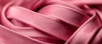 Soft pink satin ribbon folded in gentle waves creating elegant texture and shadows, macro close-up view showing fine fabric detail and luxurious sheen.