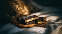 Dark chocolate pieces on wooden board with dramatic lighting and shadows, creating moody atmosphere for food photography and confectionery marketing.