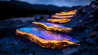 Glowing golden edges illuminate vibrant blue pools on dark rocky terrain at twilight, creating magical natural abstract patterns in mystical evening landscape.
