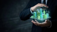 Businessman in dark suit holding glowing holographic cityscape with upward trending graphs, representing urban development, smart city technology, and financial growth in digital innovation.