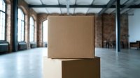 Stacked cardboard boxes in modern industrial warehouse space with natural light from large windows, suitable for logistics and shipping concepts.
