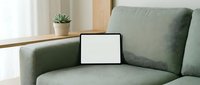 Modern green fabric sofa with blank tablet screen in minimalist living room interior for digital mockup and home office workspace design.