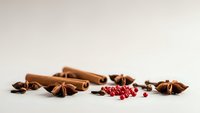 Aromatic cinnamon sticks, star anise and pink peppercorns scattered on neutral background for culinary and cooking projects.