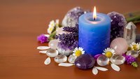 Blue candle burning surrounded by amethyst crystals, rose quartz stones, lavender flowers and chamomile creating peaceful spa meditation atmosphere.