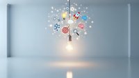 Glowing lightbulb with creative business icons floating above in modern white interior space representing innovation and brainstorming concepts.