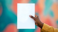 Person of African descent wearing a yellow garment holding blank white paper against colorful blurred background, suitable for advertising, marketing campaigns, and promotional materials.
