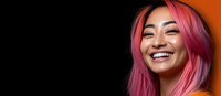 Young Asian woman with vibrant pink hair smiling joyfully against dark background, showing genuine happiness and confidence in modern beauty portrait.