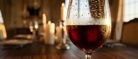 Glass of red wine with condensation droplets on elegant dining table with warm candlelight creating romantic atmosphere for dinner celebration.