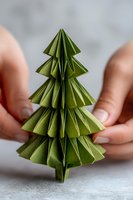 Green origami Christmas tree held in hands against neutral background. Perfect for holiday crafting and sustainable decoration ideas.