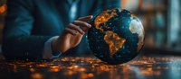 Glowing world globe with illuminated city lights at night showing South America and Africa continents, with hand reaching towards Earth model on dark surface.