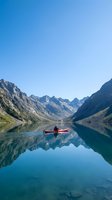 Man in red kayak paddling on calm alpine lake surrounded by towering mountain peaks reflected in still water under clear blue sky, suitable for travel and outdoor recreation marketing.