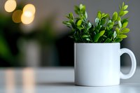 Fresh green boxwood sprigs arranged in white ceramic coffee mug on table with soft bokeh lights in background, creating minimalist home decor atmosphere.