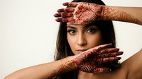 Young South Asian woman with intricate henna mehndi patterns on hands, posing gracefully against white background for cultural and beauty concepts.
