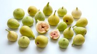 Fresh green figs arranged on white background with cut halves showing pink flesh. Organic Mediterranean fruit for healthy eating and cooking recipes.