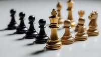 Chess pieces arranged in battle formation with golden king in focus representing strategy and leadership in business competition.