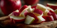 Fresh red apple slices on wooden cutting board, showcasing crisp white flesh and vibrant skin for healthy snacking or cooking preparation.