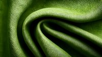 Elegant green fabric with soft folds and textured surface creates dynamic waves and shadows, showcasing luxurious textile material for fashion and interior design.