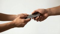 Two people with dark skin tone exchanging a smartphone against a neutral background, representing technology sharing, communication, or mobile device transfer.