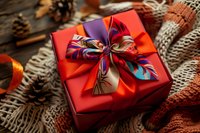 Red gift box with colorful ribbon bow on cozy knitted background with pine cones and autumn decorations for holiday season celebrations.