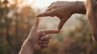 Male hands forming frame gesture against warm sunset light creating natural viewfinder for photography composition and creative vision planning outdoors.