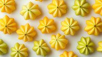 Yellow and green flower-shaped butter cookies arranged in rows on white background, isolated sweet dessert pattern for bakery and confectionery design.