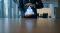 Business professional hands forming protective triangle over miniature house model on office desk symbolizing property insurance and real estate security.