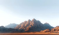 Majestic mountain peaks glowing orange at sunrise over vast desert plain, dramatic natural landscape with rugged rocky formations and clear morning sky.
