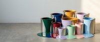 Colorful metallic paint cans in various sizes arranged on concrete floor against neutral wall background for home renovation and decorating projects.