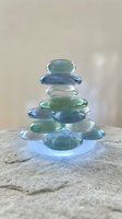 Stacked translucent glass stones in shades of blue and green arranged in pyramid formation on stone surface, symbolizing balance and wellness.