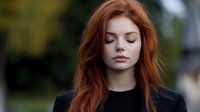 Young redhead woman with closed eyes and serene expression wearing black top against blurred natural background, showing peaceful contemplative moment.