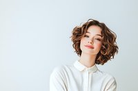 Young Asian woman with short curly brown hair smiling confidently against light background. Natural makeup, wearing white collared shirt. Modern casual business portrait.