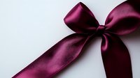 Elegant burgundy satin bow with long tails against white background, luxurious fabric texture and soft shadows create sophisticated decorative element.