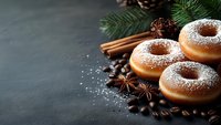 Sugar powdered donuts with coffee beans, star anise, cinnamon sticks and pine branches on dark background. Winter holiday baking and dessert concept.