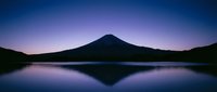 Majestic volcanic mountain silhouette reflected in calm lake waters during twilight hours, showcasing serene nature landscape for travel and environmental design projects.