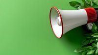 White and red megaphone with green leaves on vibrant green background. Announcement and communication concept for marketing and promotion campaigns.